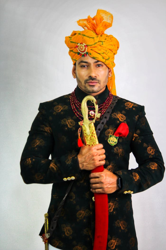 Elegant Indian groom in traditional Rajput attire holding a sword, showcasing cultural heritage.